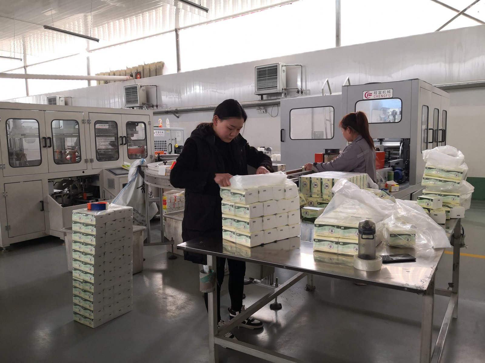 Workers stacking printed facial tissue soft packs into bundles at the packing table
